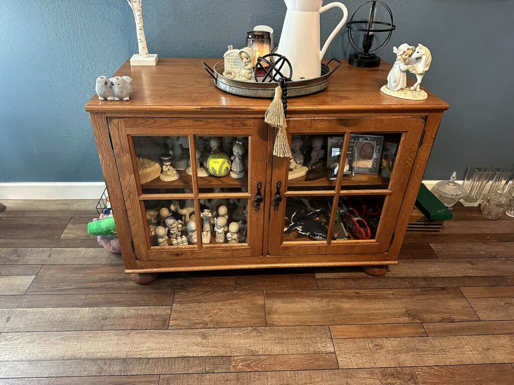 Oak glass-front cabinet with Precious Moments figurines and enamel pitcher